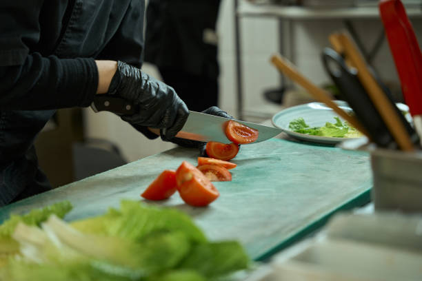 Kitchen worker cuts fresh tomatoes for a vegetable salad, washed Chinese cabbage leaves nearby